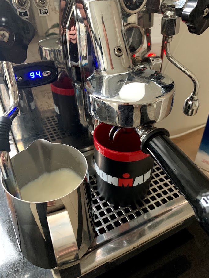 Close-up of a chrome espresso machine with portafilter, steaming pitcher, and cup on the drip tray.