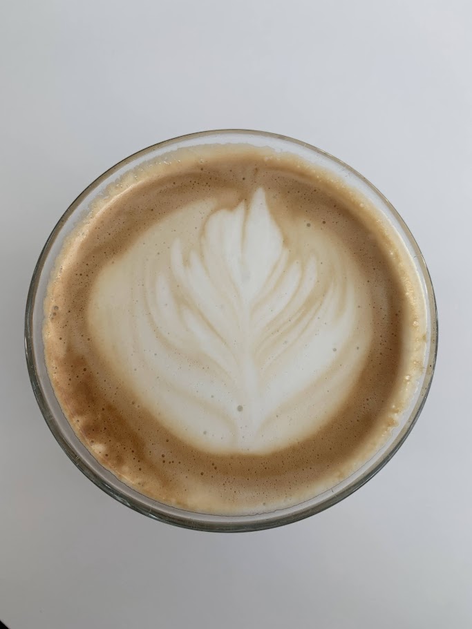 Top-down close-up of a glass of coffee with leaf-shaped latte art.